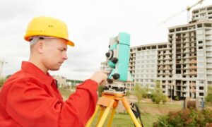 Land surveyor using surveying equipment to measure a property near a construction site