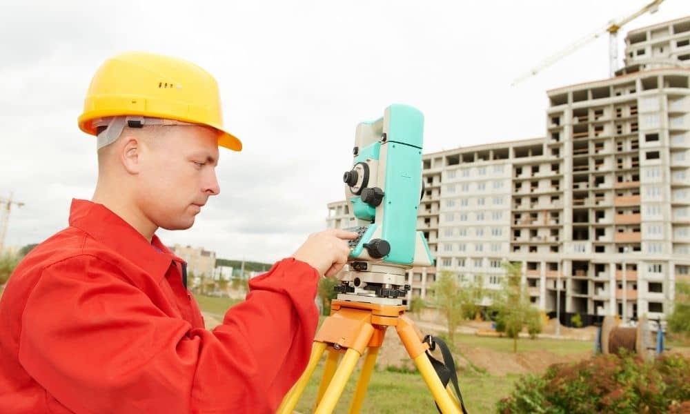 Land surveyor using surveying equipment to measure a property near a construction site